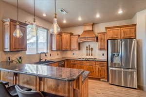 Kitchen featuring pendant lighting, sink, premium range hood, stainless steel appliances, and light wood-type flooring