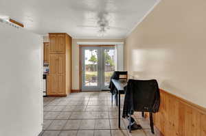 Tiled dining room featuring crown molding, ceiling fan, wooden walls, and a textured ceiling