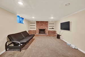 Carpeted living room with ornamental molding, a brick fireplace, a textured ceiling, and built in shelves