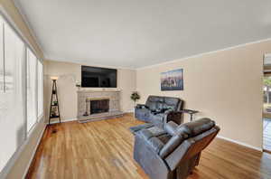 Living room with crown molding, a stone fireplace, and hardwood / wood-style floors