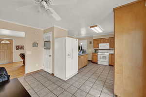 Kitchen featuring light tile patterned flooring, ornamental molding, ceiling fan, and white appliances