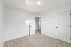 Unfurnished bedroom with a closet, light colored carpet, visible vents, and baseboards