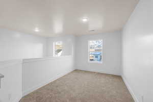 Empty room with light carpet, a textured ceiling, visible vents, and baseboards