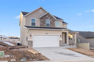 View of front facade featuring central air condition unit, stone siding, concrete driveway, and stucco siding