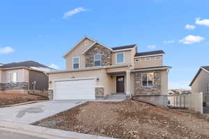 View of front facade featuring driveway, stone siding, an attached garage, fence, and stucco siding