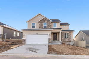 View of front facade featuring stone siding, concrete driveway, and stucco siding