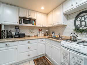 Kitchen with white cabinetry, sink, white gas range oven, and decorative backsplash