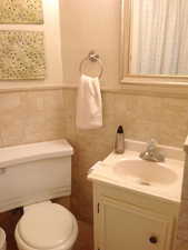 Bathroom featuring vanity, toilet, and tile walls