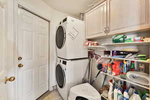 Washroom with stacked washer and dryer, cabinets, a textured ceiling, and light tile patterned flooring