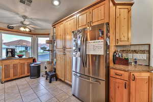 Kitchen with stainless steel refrigerator, tasteful backsplash, light tile patterned floors, light stone countertops, and a textured ceiling