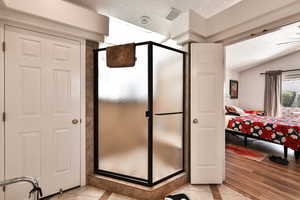 Bathroom featuring a shower with door, vaulted ceiling, tile patterned floors, and a textured ceiling