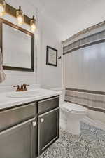 Full bathroom featuring vanity, toilet, shower / tub combo, and a textured ceiling