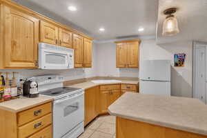 Kitchen with pendant lighting, sink, crown molding, white appliances, and light tile patterned floors