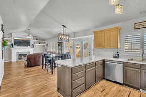 Kitchen with pendant lighting, light hardwood / wood-style floors, light brown cabinetry, stainless steel dishwasher, and kitchen peninsula