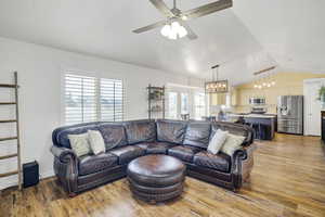 Living room featuring vaulted ceiling, ceiling fan with notable chandelier, and hardwood / wood-style floors