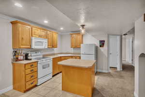 Kitchen featuring light tile patterned flooring, a center island, white appliances, crown molding, and a textured ceiling