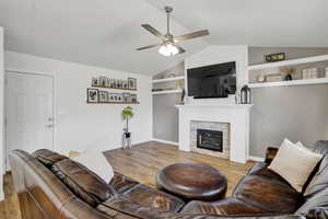 Living room featuring ceiling fan, lofted ceiling, built in features, and light hardwood / wood-style floors