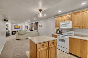 Kitchen with white appliances, a center island, a textured ceiling, light carpet, and light brown cabinets