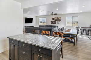 Kitchen with a kitchen island, light wood-type flooring, ceiling fan, a breakfast bar, and dark brown cabinets