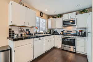 Kitchen with white cabinetry, dark hardwood / wood-style floors, tile counters, stainless steel appliances, and backsplash