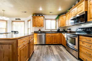 Kitchen featuring sink, appliances with stainless steel finishes, hardwood / wood-style floors, a textured ceiling, and decorative light fixtures