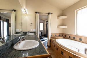 Bathroom with a relaxing tiled tub, vanity, tile patterned flooring, and vaulted ceiling