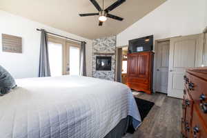 Bedroom with french doors, wood-type flooring, vaulted ceiling, ceiling fan, and a fireplace