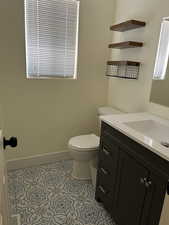 Half bath featuring toilet, tile patterned flooring, baseboards, and vanity