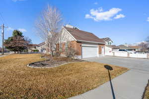 View of side of home with fence, a yard, a chimney, concrete driveway, and a garage