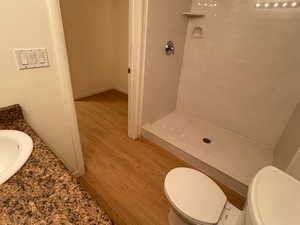 Bathroom featuring wood-type flooring, toilet, vanity, and a shower