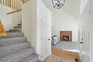 Staircase featuring wood finished floors, visible vents, high vaulted ceiling, an inviting chandelier, and a brick fireplace