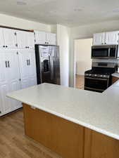 Kitchen with stainless steel appliances, light wood finished floors, light countertops, and white cabinetry