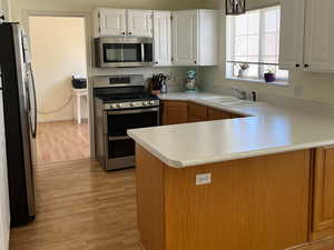 Kitchen with a sink, light countertops, a peninsula, stainless steel appliances, and light wood-style flooring