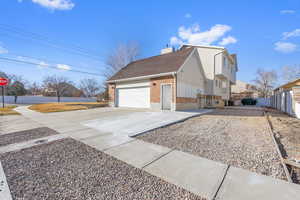 View of side of home featuring fence, concrete driveway, a garage, brick siding, and a chimney