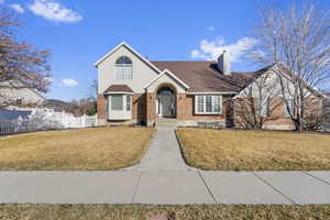 View of front of property with brick siding, a chimney, a front lawn, and fence