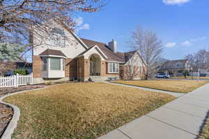 View of front of home featuring brick siding, a chimney, a front yard, and fence