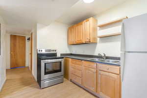 Kitchen with a sink, dark countertops, freestanding refrigerator, light wood-style floors, and stainless steel electric range