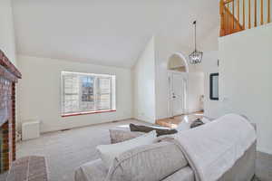 Carpeted living area with a notable chandelier, a brick fireplace, high vaulted ceiling, and baseboards