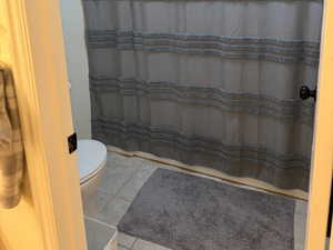 Bathroom with tile patterned floors, toilet, and a shower with shower curtain