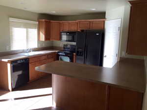 Kitchen featuring light tile patterned flooring, kitchen peninsula, sink, and black appliances