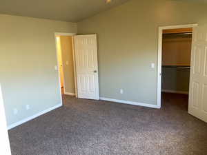 Unfurnished bedroom featuring lofted ceiling, a walk in closet, a closet, and dark colored carpet