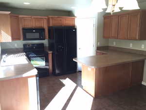 Kitchen with dark tile patterned floors, kitchen peninsula, sink, and black appliances