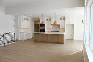 Kitchen featuring a large island, white cabinetry, hanging light fixtures, black appliances, and decorative backsplash