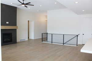 Unfurnished living room featuring a tile fireplace, ceiling fan, and light hardwood / wood-style flooring