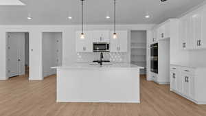 Kitchen with stainless steel appliances, white cabinetry, pendant lighting, and a center island with sink