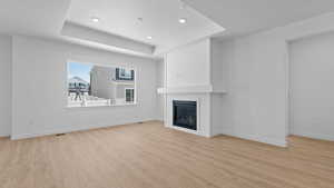 Unfurnished living room with light hardwood / wood-style floors, a fireplace, and a tray ceiling