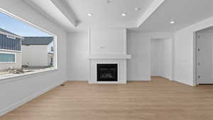 Unfurnished living room with a fireplace, a tray ceiling, and light hardwood / wood-style flooring