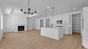 Kitchen featuring sink, light hardwood / wood-style flooring, hanging light fixtures, an island with sink, and white cabinets