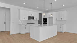 Kitchen with tasteful backsplash, decorative light fixtures, white cabinets, and a center island with sink