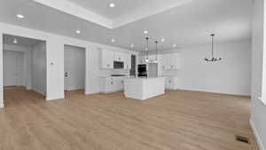 Kitchen with a center island with sink, white cabinets, light wood-type flooring, and decorative light fixtures